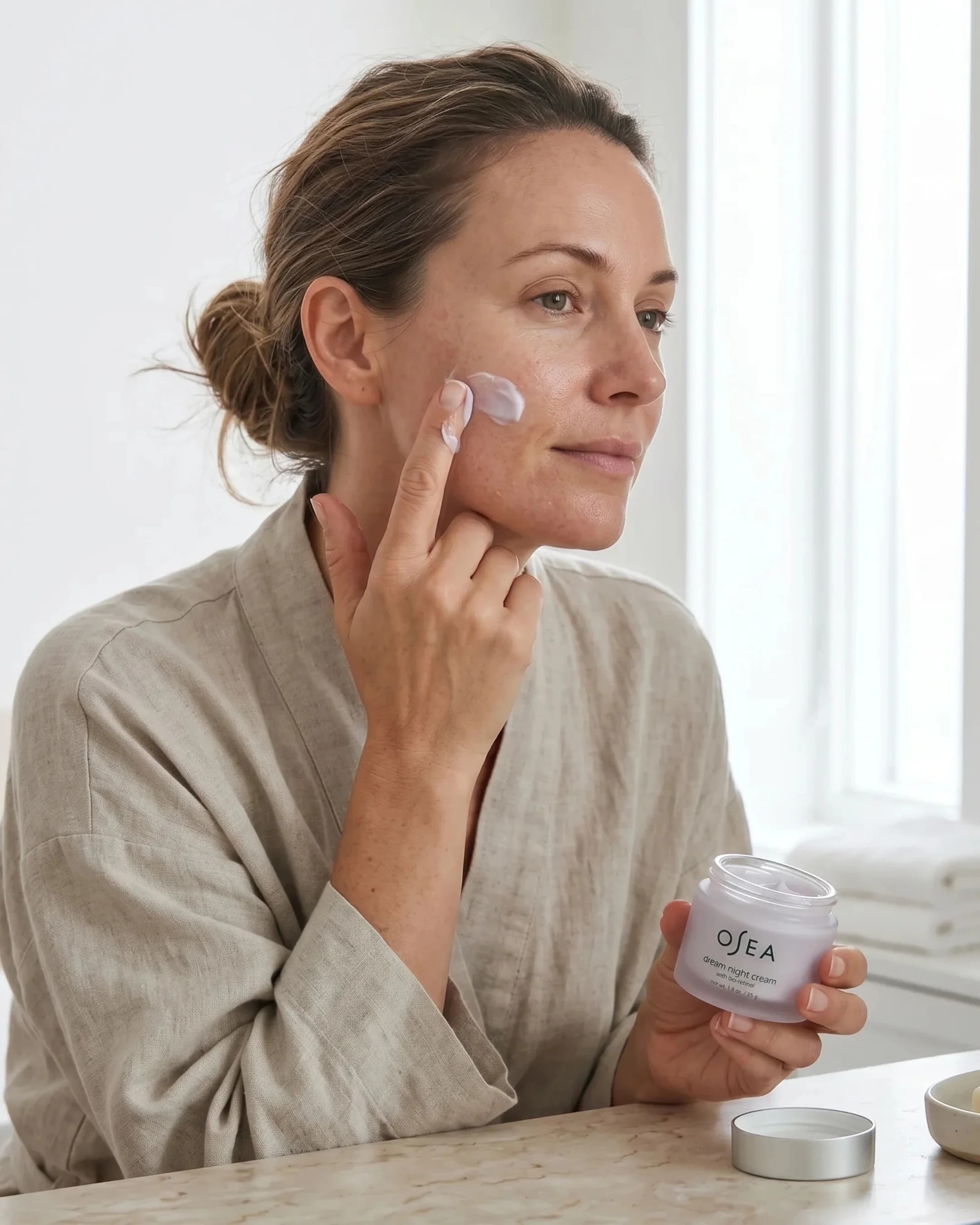 Woman applying face cream in a linen robe — AI skincare product photography for ecommerce beauty brands
